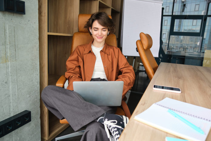 Portrait of young female manager, working woman in office, using laptop, typing on computer