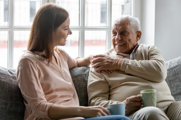 Smiling,Young,Woman,Sitting,On,Sofa,With,Happy,Older,Retired